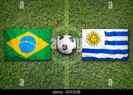 Brazil vs. Uruguay flags on green soccer field Stock Photo