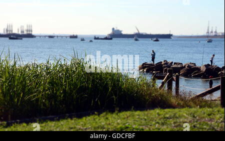 Sydney, Australia - Apr 21, 2014. People fishing on the breakwall. Tankers and Botany bay's industrial area in the background. Stock Photo