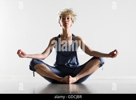 Attractive barefoot young woman sitting meditating on a white floor with a serene expression Stock Photo