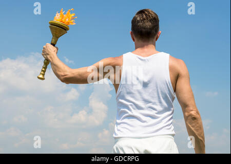 Torchbearer athlete in old fashioned white uniform holding sport torch against sunny blue sky Stock Photo