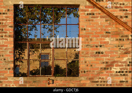 Window in a red brick wall of an old defunct shipyard in Clydebank. Looking through the glass-less window frame you can see a tenement building Stock Photo