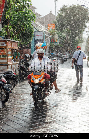 Indonesian man riding a motorbike under the rain on the street of Kuta, Bali, Indonesia. Stock Photo