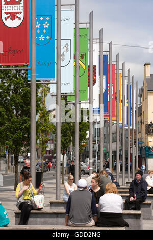 Ireland, Co Galway, Galway, Eyre Square, John Kennedy Park, visitors sat below tribe family flags Stock Photo