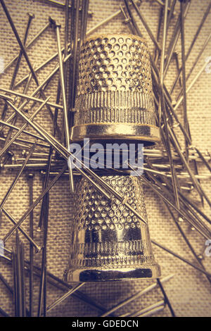 Pins and thimbles on a piece of cloth seen from above. Vintage style. Vertical  image. Stock Photo