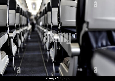 View from back of plane looking down aisleway at arms of seats as passengers board the plane with shallow depth of field Stock Photo