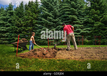 Father and son digging soil in garden Stock Photo