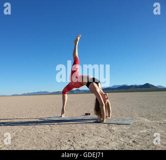 Woman doing a one legged wheel pose in a dry lake, Nevada, United States Stock Photo