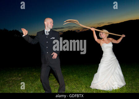 Happy bride and groom standing in a field during twilight, bride teasing the groom with a pitchfork Stock Photo