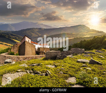 composite mountain landscape with ancient fortress with high stone walls and red roof among the woods and huge boulders on a hil Stock Photo