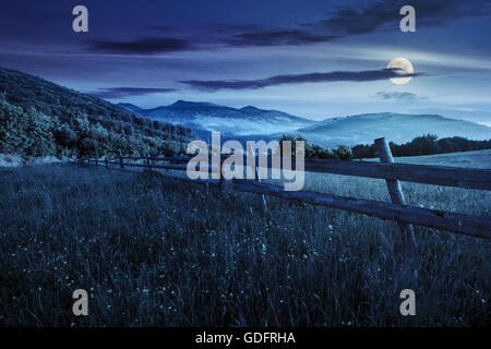 rural landscape. fence on the hillside meadow shot with ultrawideangle lense. forest in fog on the mountain top at night in full Stock Photo