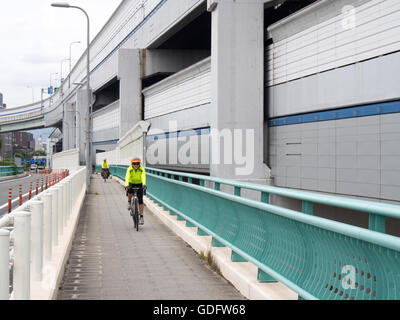 Two touring cyclists cycling on a bike path beside the Hanshin Expressway between Kobe and Osaka. Stock Photo