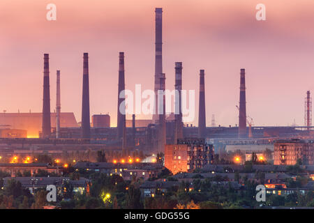 City buildings on the background of steel factory with smokestacks at night.  Metallurgical plant with chimney. steelworks, iron Stock Photo