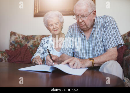Indoor shot of elderly couple at home signing paperwork together. Retired man and woman sitting on couch and going through some Stock Photo