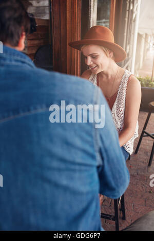 Young caucasian woman wearing hat sitting at a coffee shop with her male friend. Young friends sitting at a cafe table. Stock Photo