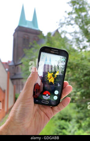 German version of the latest Nintendo game 'Pokémon go'. Pokemon monster in the garden of the church on a smartphone of a player. Dortmund, Germany, July 17th.2016 Stock Photo