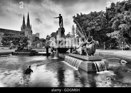 Black-white view of Hyde park in Sydney with fountain, cathedral and surrounding trees. Blurred flowing water streams of popular Stock Photo