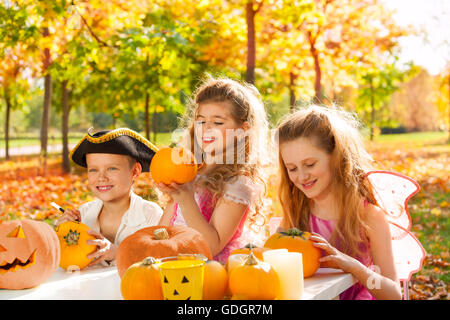 Three kids in costumes crafting Halloween pumpkins Stock Photo