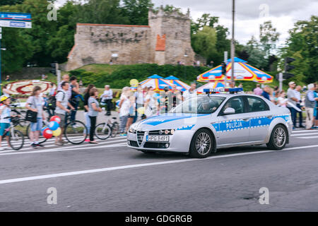 Polish police car speeding past people watching the parade with the old castle ruins in the background Stock Photo