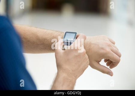 Close-up of hand of young man touching display on his smart watch with blank black screen, using internet, messaging, making cal Stock Photo