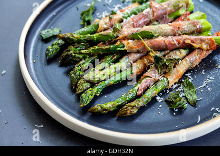 Grilled asparagus wrapped in Parma ham with parmesan, sage and thyme Stock Photo
