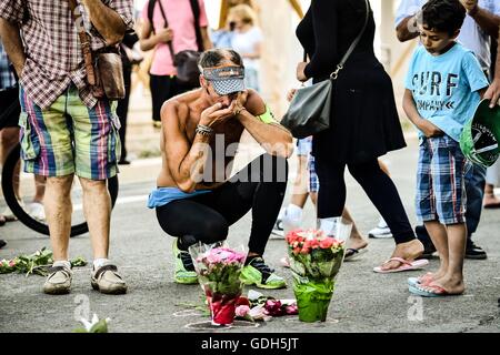 A man reacts as he kneels in front of floral tributes where bodies fell on the Promenade des Anglais, Nice, as French detectives are trying to piece together the circumstances that left at least 84 people dead and scores injured after a terrorist deliberately drove a lorry into Bastille Day revellers, before being fatally wounded in a stand-off with armed police. Stock Photo
