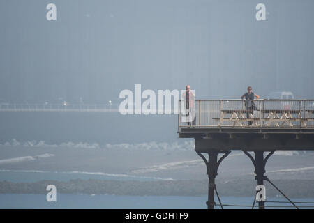 Aberystwyth Wales UK, Sunday 18 July 2016 UK weather: People on the seaside pier in Aberystwyth on a misty July summer morning . The weather is forecast to improve dramatically today and on Tuesday, with temperatures forecast to soar to over 30º centigrade in parts of the south east Credit:  Keith Morris/Alamy Live News Stock Photo