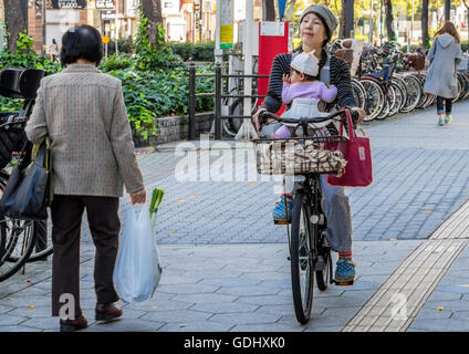 Mother with child cycling in the city of Osaka Japan along cycle paths which are generally kept separate from road traffic Stock Photo