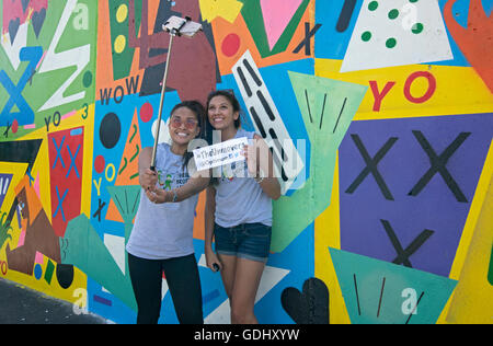 2 college students take a selfie in front of a Coney Island Art Wall to promote THE UNMOVERS, a youtube Optimum series. Stock Photo