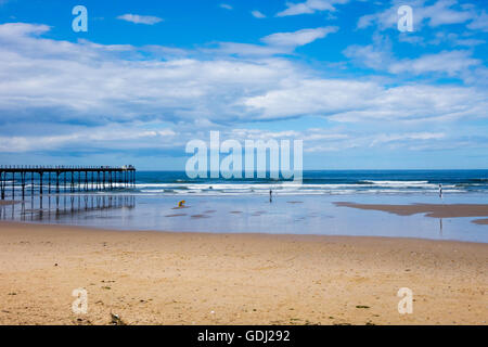 Deserted Saltburn Beach and pier with a few surfers summer sunshine blue sky  with cumulus clouds Stock Photo
