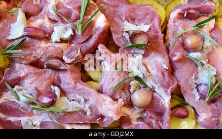 Raw pork neck chops with potatoes slices, rosemary and garlic in pan. The meal is prepared for baking. Stock Photo