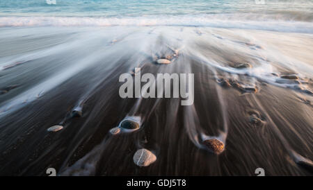 Pebbles in the beach on a black sand and flowing sea water creating nice textures. Long exposure image. Stock Photo