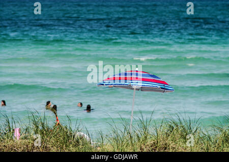 Blue and red umbrella with the ocean and bathers in the background - South Beach in Miami Stock Photo