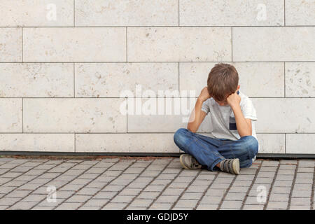 Sad, lonely, unhappy, upset, disappointed tired child sitting alone on the ground Outdoor Stock Photo