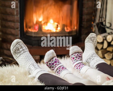 Warming and relaxing near fireplace. Woman and child feet in front of fire. Stock Photo