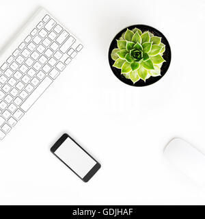 White office desk table with wireless aluminum keyboard, smart phone with blank screen, mouse and succulent flower in pot. Top v Stock Photo