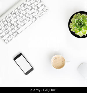 White office desk table with wireless aluminum keyboard, cup of coffee, smart phone with blank screen, mouse and succulent flowe Stock Photo
