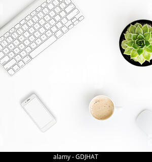 White office desk table with wireless aluminum keyboard, cup of coffee, smart phone with blank screen, mouse and succulent flowe Stock Photo