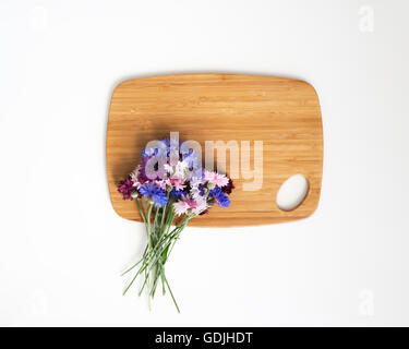 Wooden cutting board with decoration of flowers on white background. Overhead view. Flat lay. Stock Photo