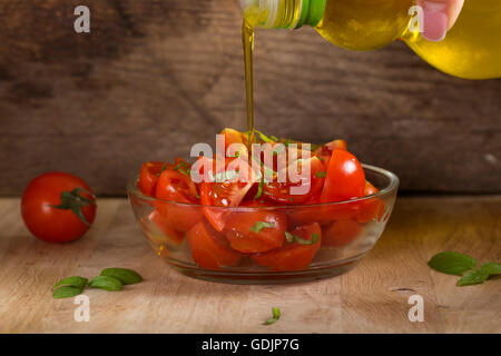 Pouring olive oil over sliced tomatoes in bowl on old rustic wooden background Stock Photo