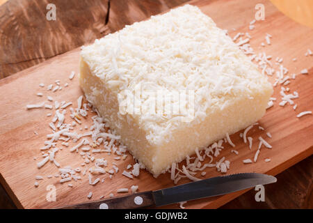 Brazilian traditional dessert: sweet couscous (tapioca) pudding (cuscuz doce) with coconut on wooden board. Selective focus Stock Photo