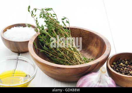 Cooking ingredients: thyme, salt, pepper, chili, garlic, olive oil in bowls on white rustic wooden table Stock Photo