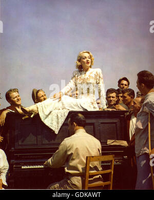 Marlene Dietrich sitting on a piano with G.I.'s and wounded soldiers gathered around listening to her sing. Picture taken at an evacuation hospital area near the front lines in Italy. Stock Photo