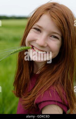 Smiling teenage girl, laughing, with barley grass in her mouth, Germany Stock Photo