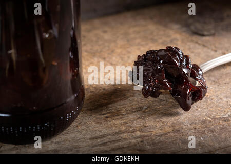 Cherry jam in spoon and one preserving glass jar over old wooden rustic background Stock Photo