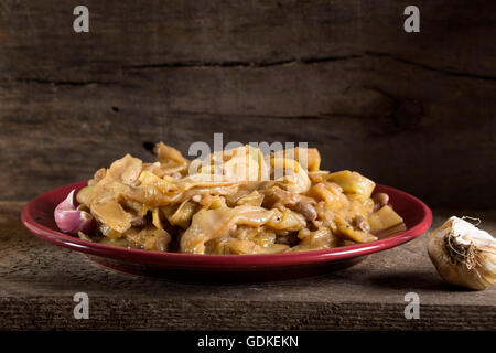 Cooked broad bean pods with garlic on red plate over wooden rustic background Stock Photo