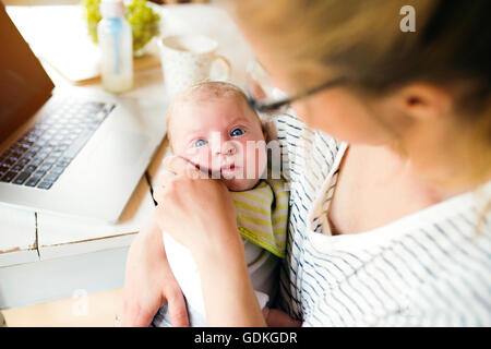 Unrecognizable mother holding baby son, milk in bottle, laptop Stock Photo