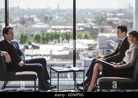 Business people sitting near panoramic window with view on city and talking Stock Photo