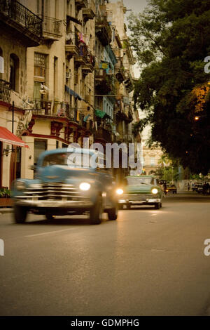 Sunset on a historic street with tall historic apartment houses and classic American cars in downtown Havana, Cuba. Stock Photo