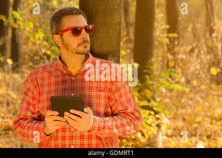 Man with a digital tablet leaning against the tree Stock Photo