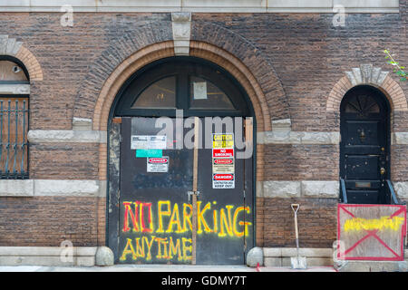 New York City building brick facade under construction with permits, warnings and No parking anytime spray painted on doors. Stock Photo